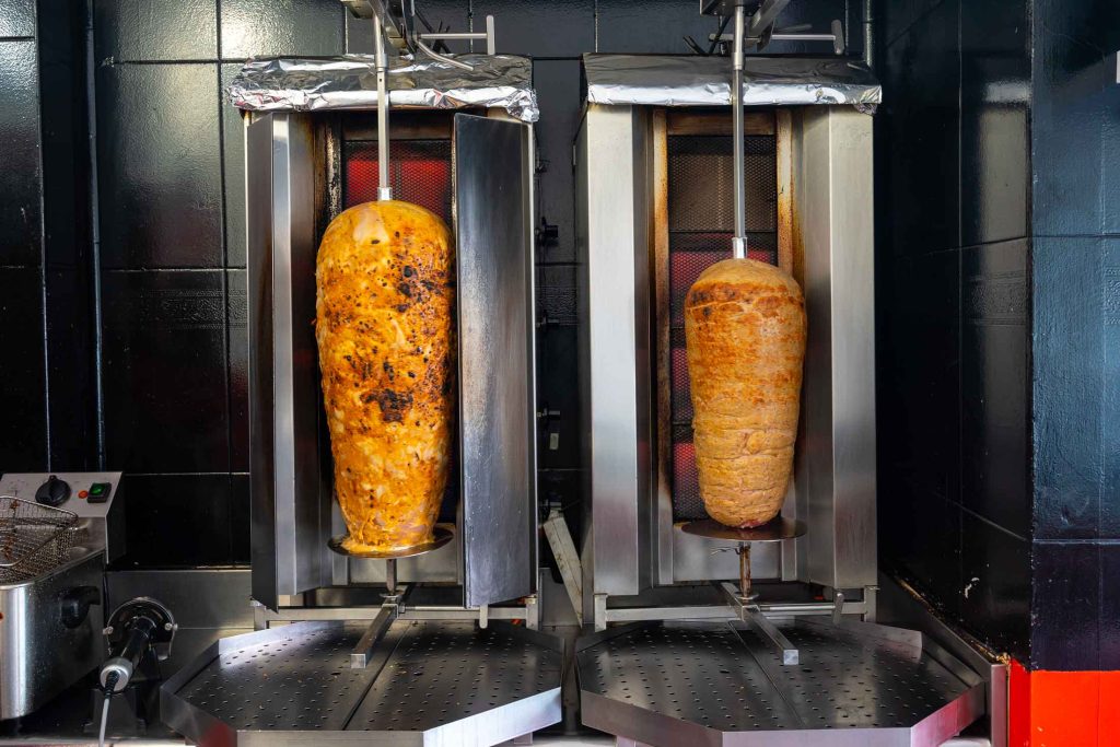 Deux machines à kebab avec des broches de viande grillant dans un restaurant.