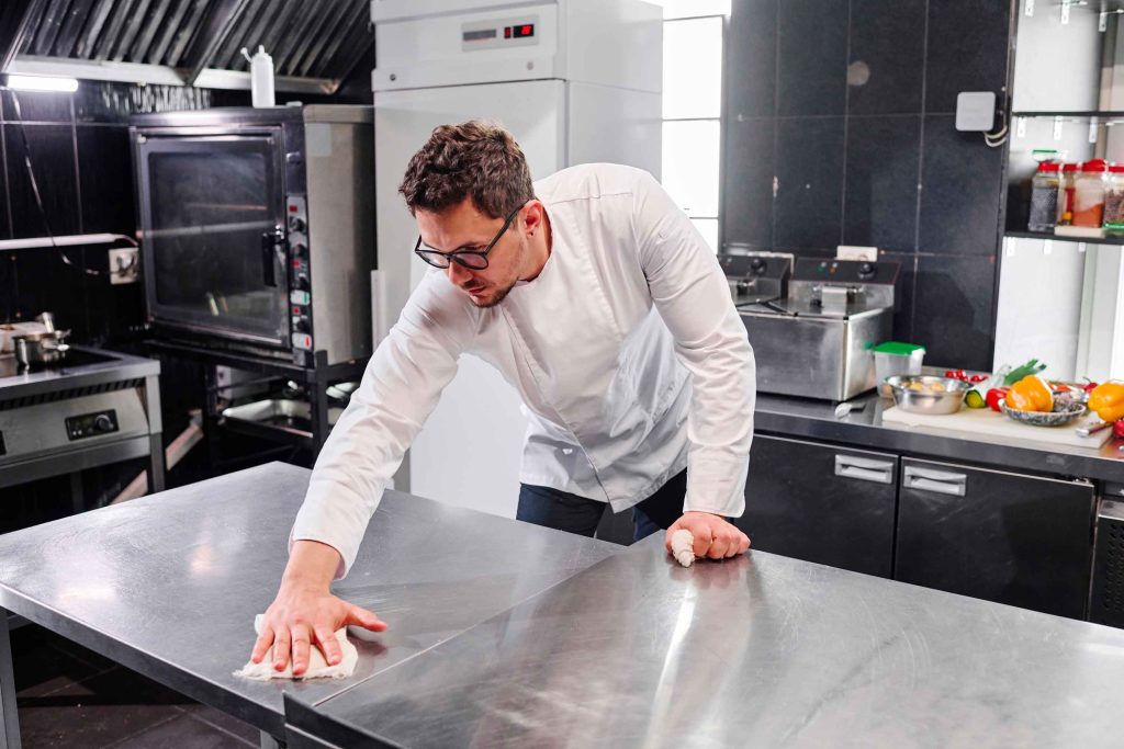 Chef nettoyant une plancha professionnelle dans une cuisine de restaurant.