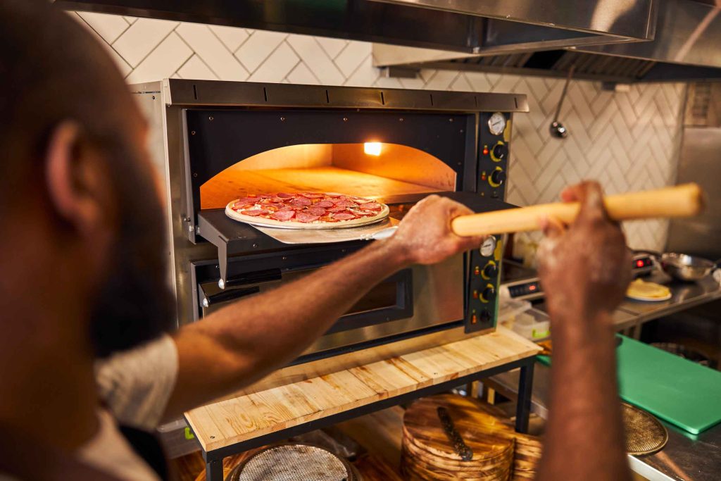 Cuisinier utilisant un four à pizza professionnel dans une cuisine de restaurant.