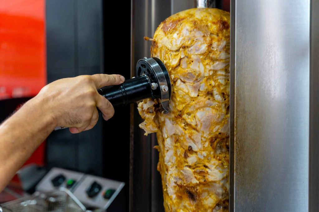 Coupe d’une broche de poulet à l’aide d’un couteau électrique pour kebab professionnel.