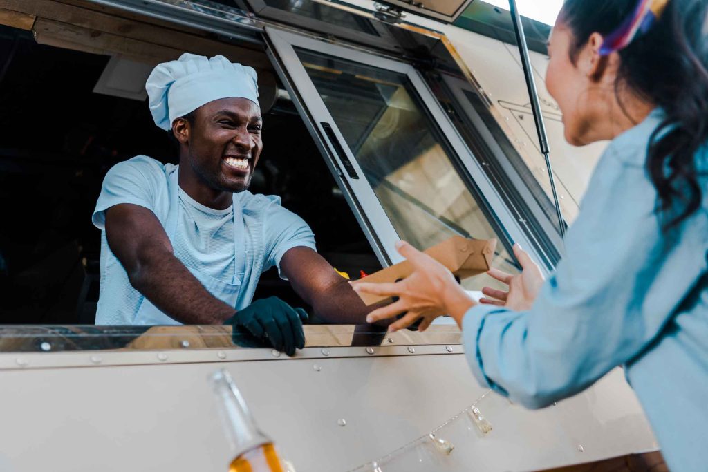 Chef de food truck souriant servant une cliente avec enthousiasme.
