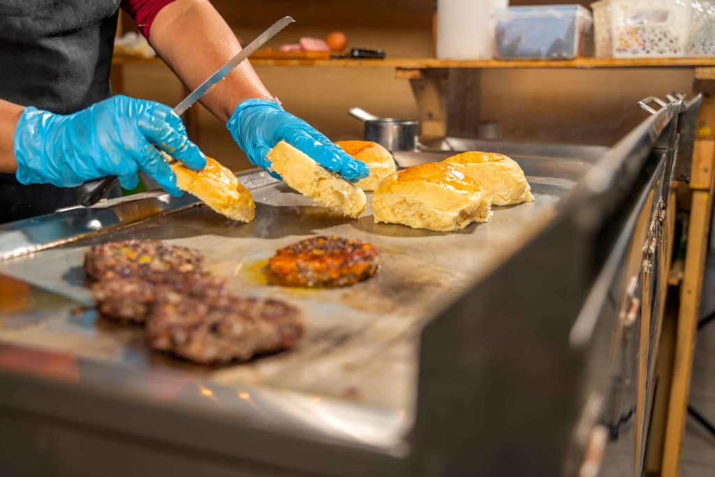 Cuisson de pains et steaks hachés sur une plancha pour la préparation de burgers dans un restaurant rapide.